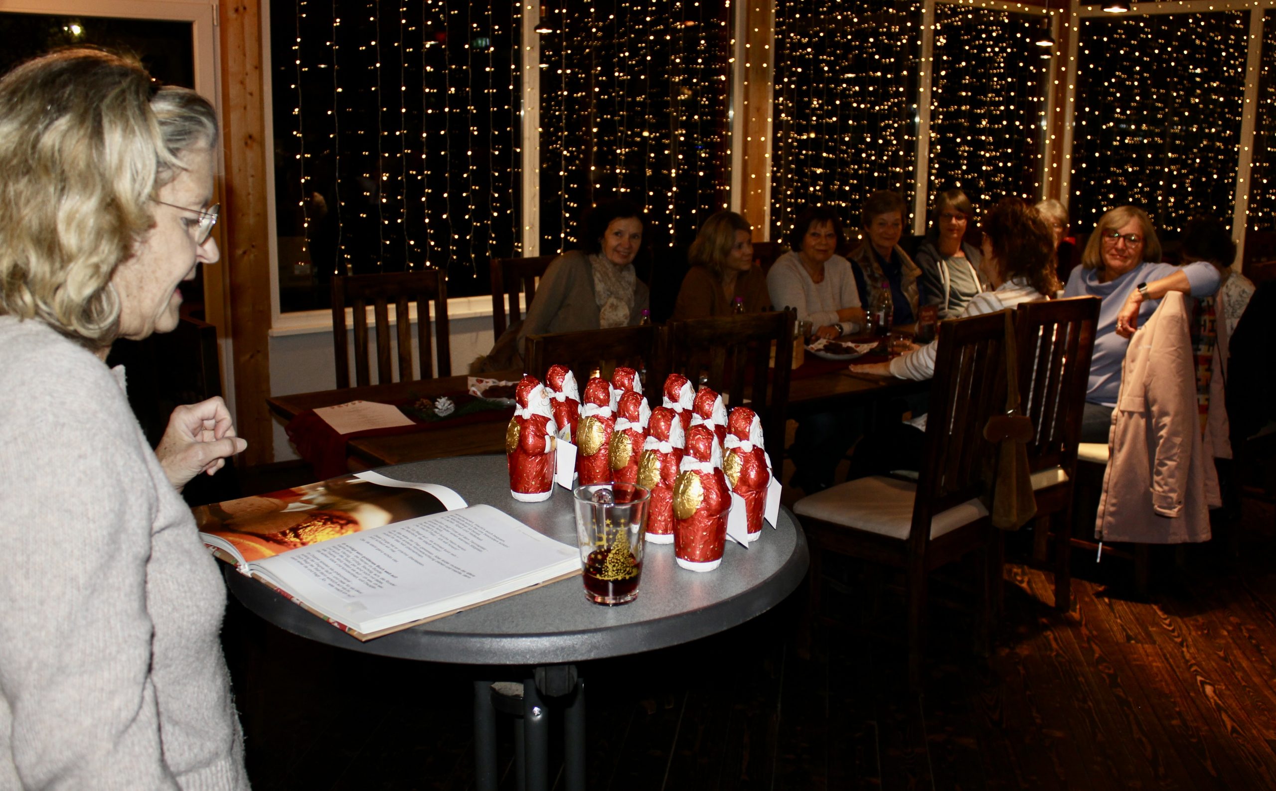 Das Bild zeigt Petra Heß (links) vor einer Gruppe von Schoko-Nikoläusen und die Zuhörerinnen im Hintergrund