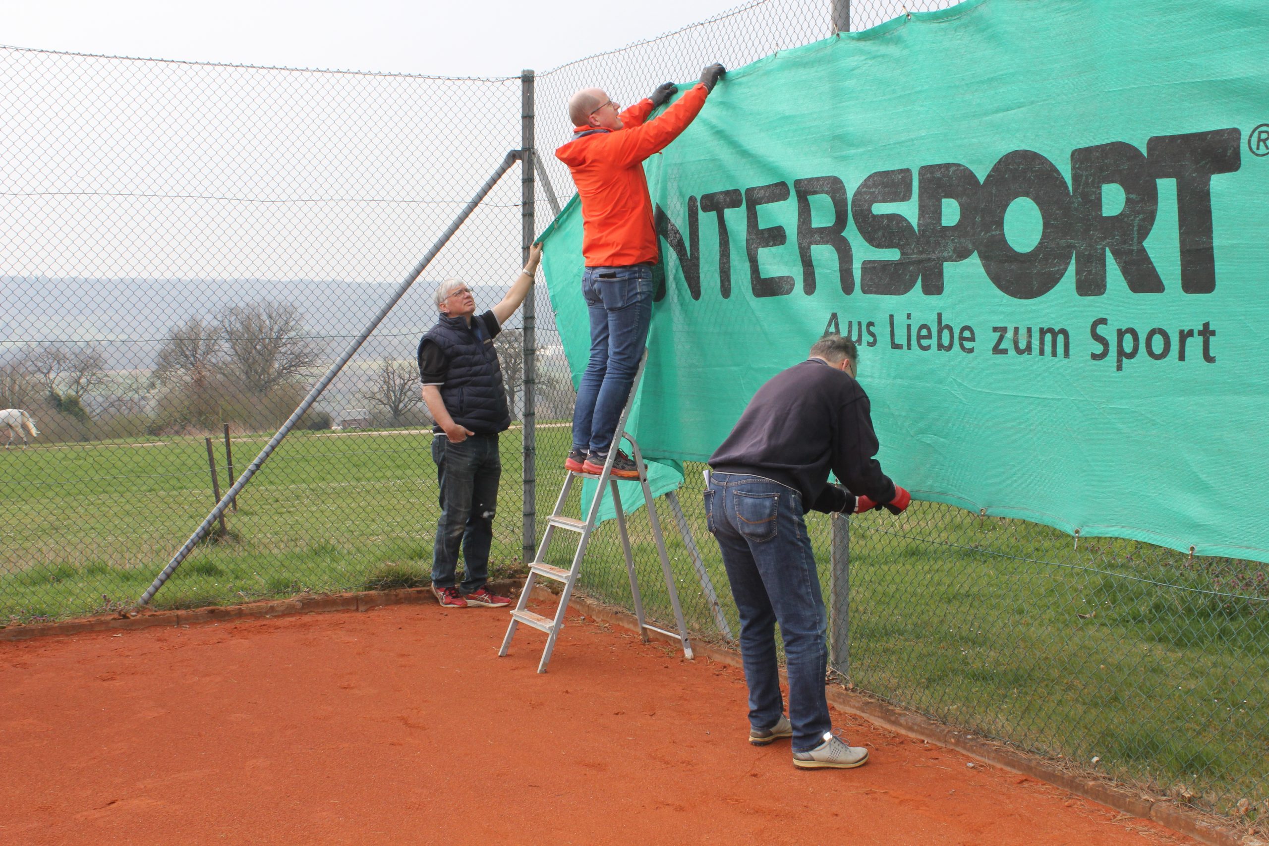Das Bild zeigt Helfer beim Anbringen der Sichtblenden auf den Tennisplätzen